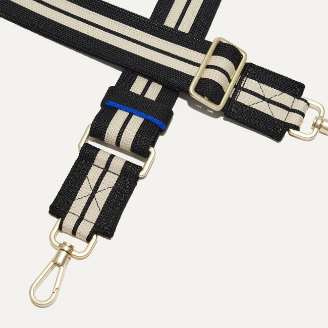 A closeup of The Crossbody Strap in Black and White Stripe, focusing on the end snap hooks and sliding buckle.