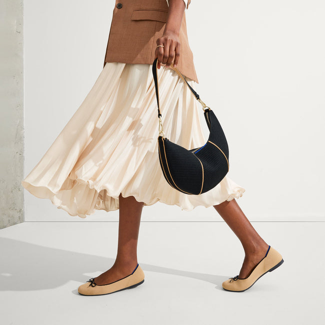 Another view of model holding The Crescent Bag in Black by the shoulder strap, shown in motion. 