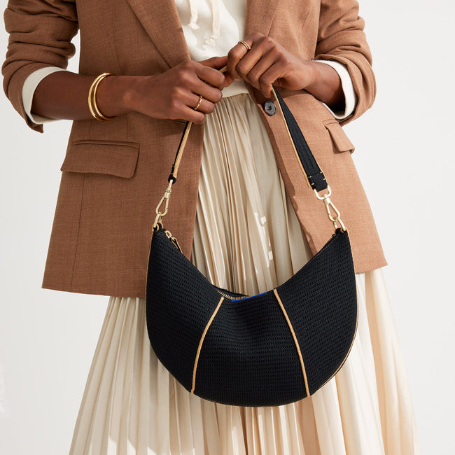 Model holding The Crescent Bag in Black by the shoulder strap, shown from the front.