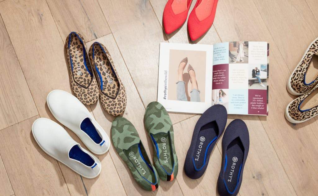 An assortment of solid and patterned Rothy's shoes on a wooden floor, shown from the top.