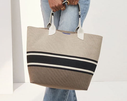 A woman is seen holding a fashionable tote bag, highlighting her elegance and the bag's functional design.  