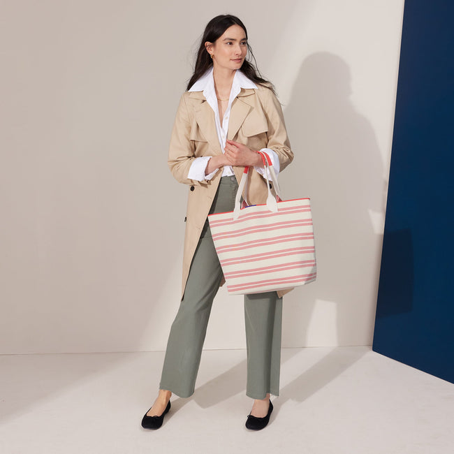 An alternate view of model holding The Lightweight Tote in Coral Stripe.