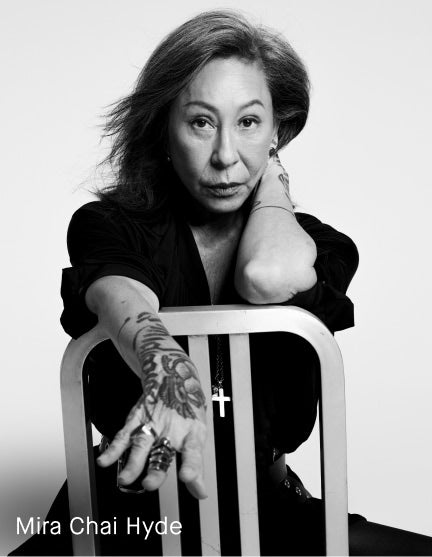 Black and white portrait of artist Mira Chai Hyde leaning on a metal chair, with her name printed in white text at the bottom left.