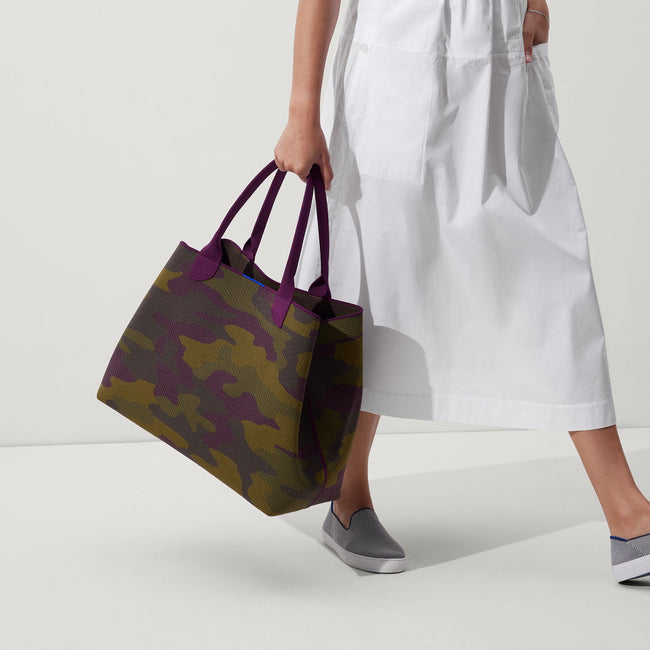 The Lightweight Mega Tote in Legacy Camo, carried by its top handles by a model, shown in motion from the side.