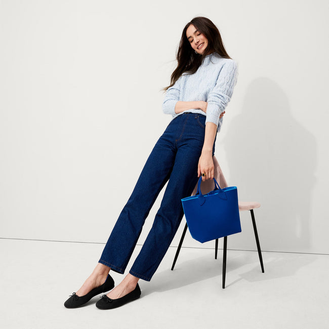 The Lightweight Petite Tote in French Blue, carried by its top handles by a model, shown from front.