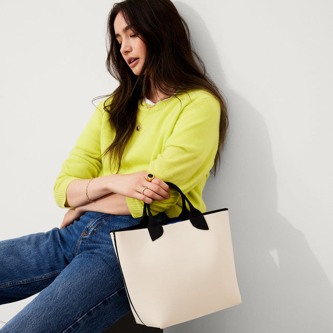 The Lightweight Petite Tote in Vanilla Cream, carried by its top handles by a model, shown from front.