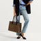 The Classic Tote in Toasty Cat, carried by its top handles by a model, shown from side.