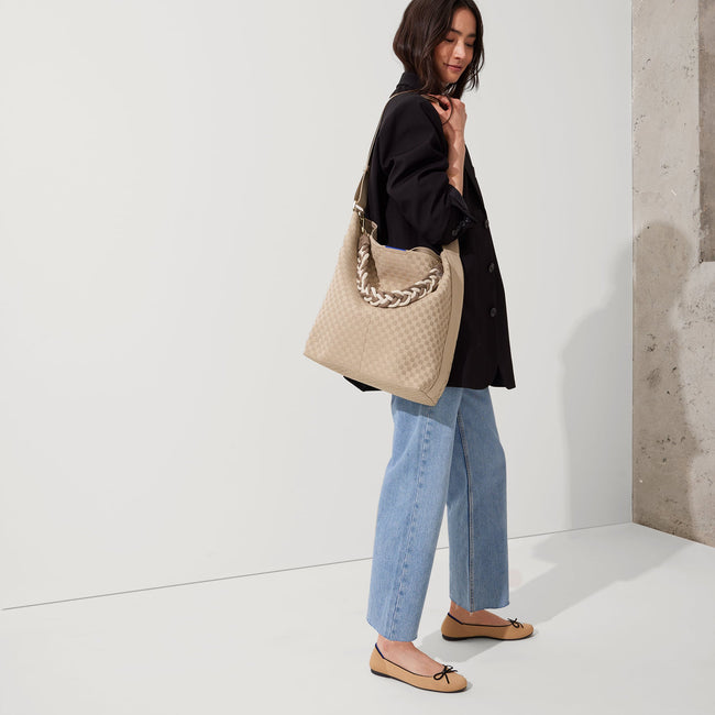 The Braided Shoulder Strap in Cream & Cocoa, shown paired with The Bucket Bag, worn by a model and shown from the side. 