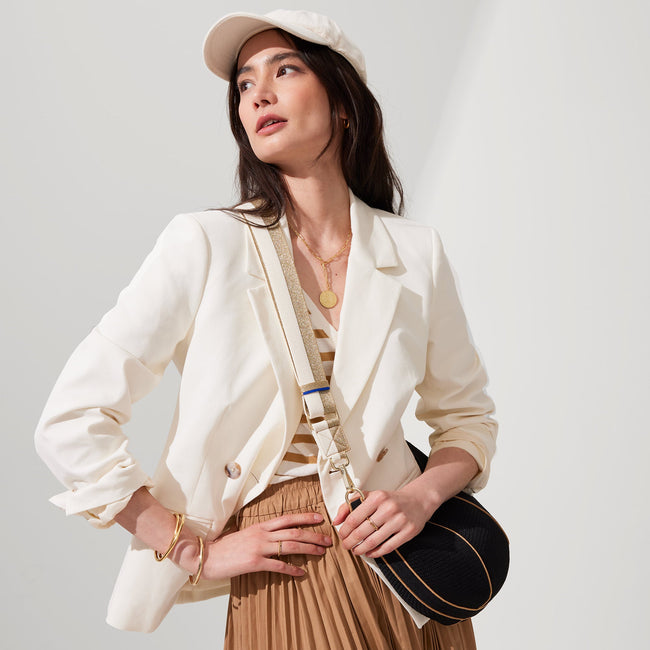 The Crossbody Strap in Gold and White, shown paired with The Crescent Bag, worn by a model, shown from the side.
