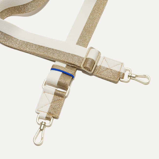 A close-up of The Crossbody Strap in Gold and White, focusing on the end snap hooks and sliding buckle.