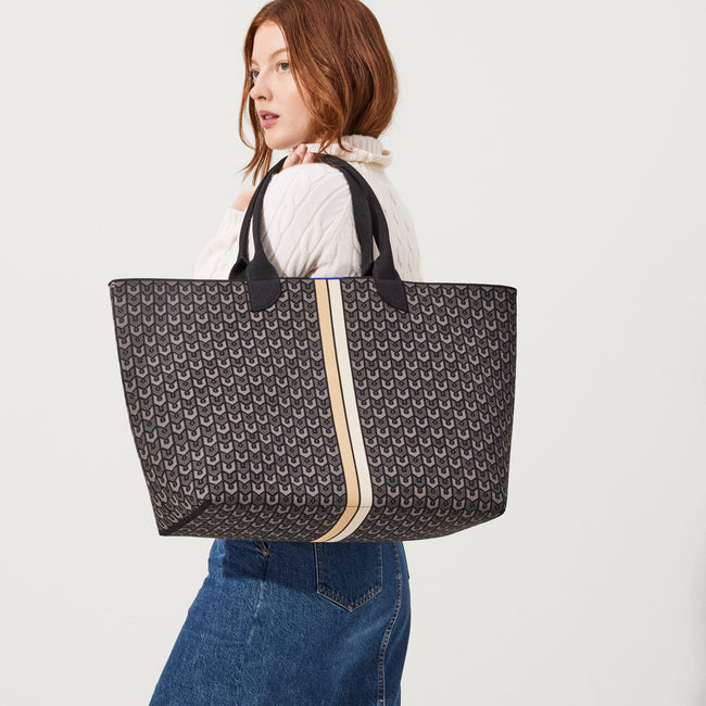 The Reversible Lightweight Mega Tote in Signature Black, carried by its top handles by a model, shown from the front. 