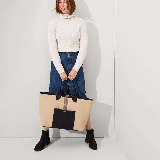 The Reversible Lightweight Mega Tote in Signature Black, carried by its top handles by a model, shown from the front, with the reverse side showing.