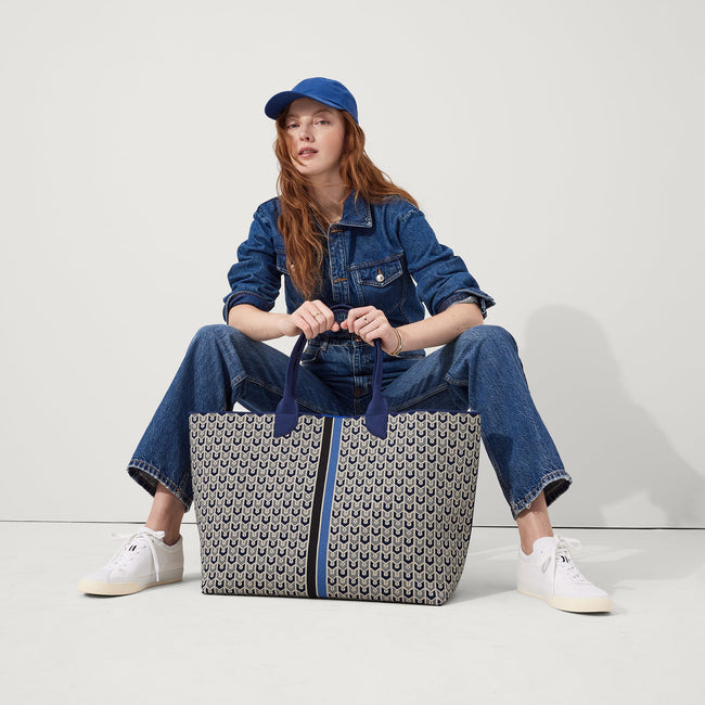 The Lightweight Mega Tote in Signature Blue, carried by its top handles by a model, shown from the front.