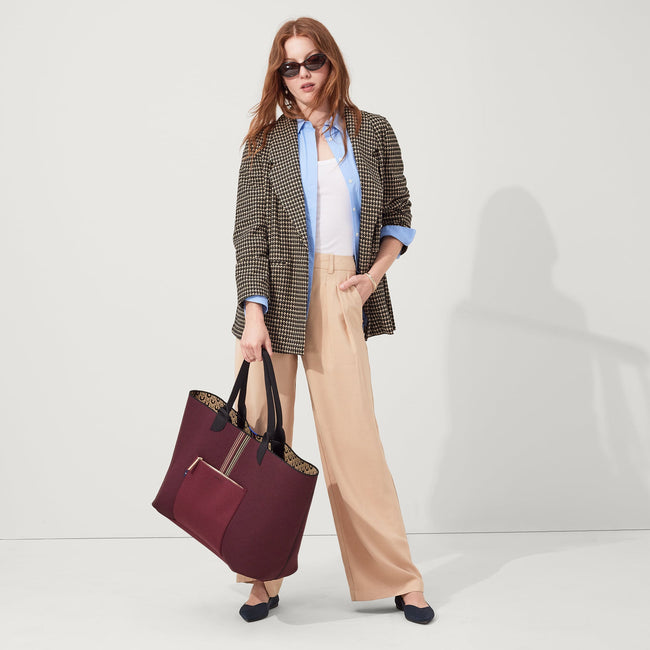 The Lightweight Mega Tote in Signature Brown, carried by its top handles by a model, shown from the front. 