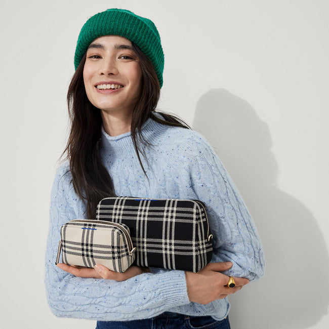 Model shown holding the large and small pouch of The Universal Pouch Set in Black and Cream Plaid.