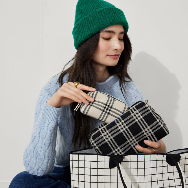 Model shown holding the large and small pouch of The Universal Pouch Set in Black and Cream Plaid.