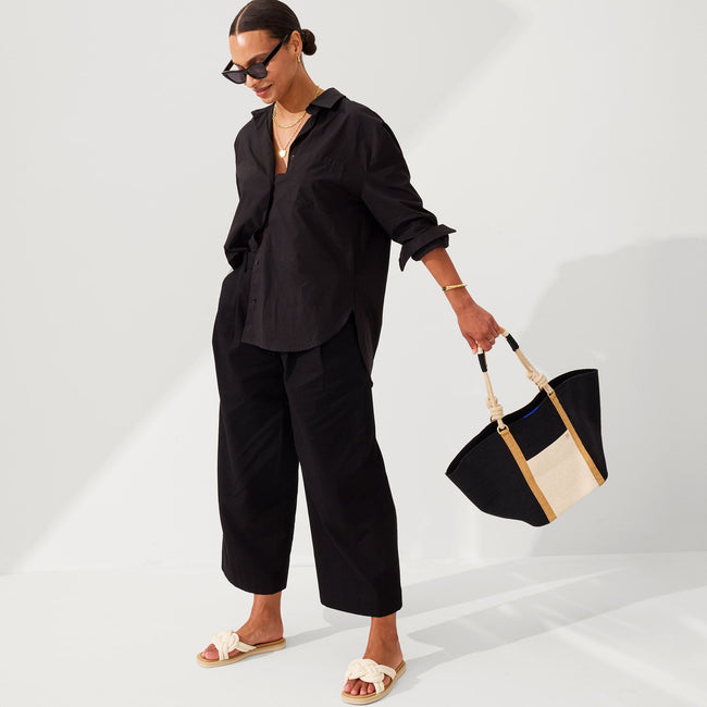 An alternate view of a model holding The Reversible Summer Tote in Black.