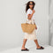 An alternate view of a model holding The Summer Tote in Camel.