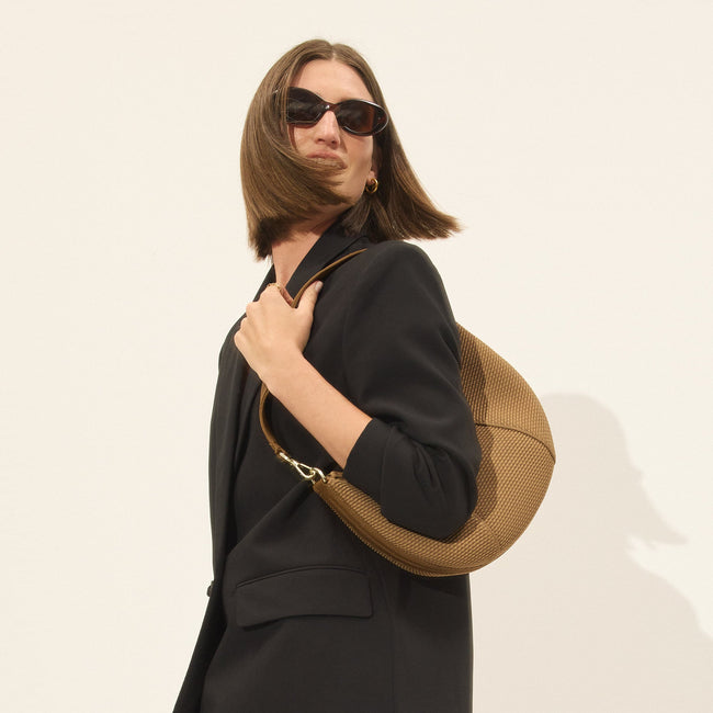 Model holding The Crescent Bag in Horizon by the shoulder strap, shown from the front.