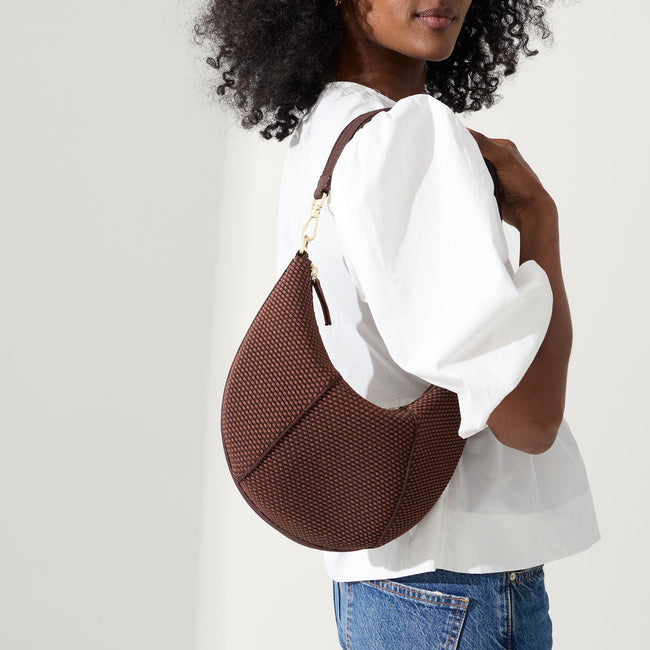 Model holding The Crescent Bag in Eclipse by the shoulder strap, shown from the front.