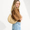 hover | Model holding The Crescent Bag in Brown Butter by the shoulder strap, shown from the front.