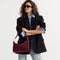 The Daily Crossbody in ReVelvet™ Syrah , carried over the shoulder of a female model, shown from the right.