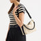 The Daily Crossbody in Black and White Raffia-Knit, carried over the shoulder of a female model, shown from the right.