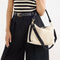 hover | The Daily Crossbody in Black and White Raffia-Knit, carried over the shoulder of a female model, shown from the right.