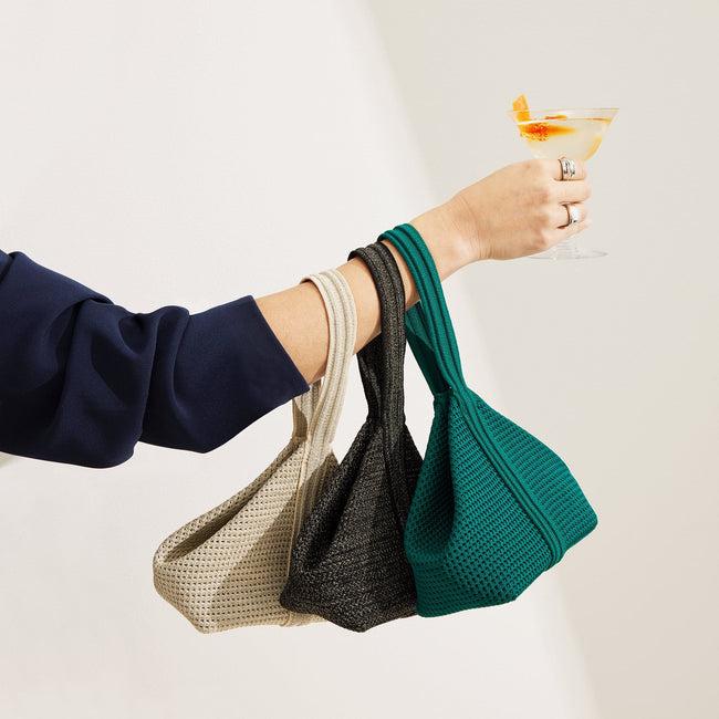 An image of a model's arm holding all three colorways of The Party Pouch with a cocktail in hand. 