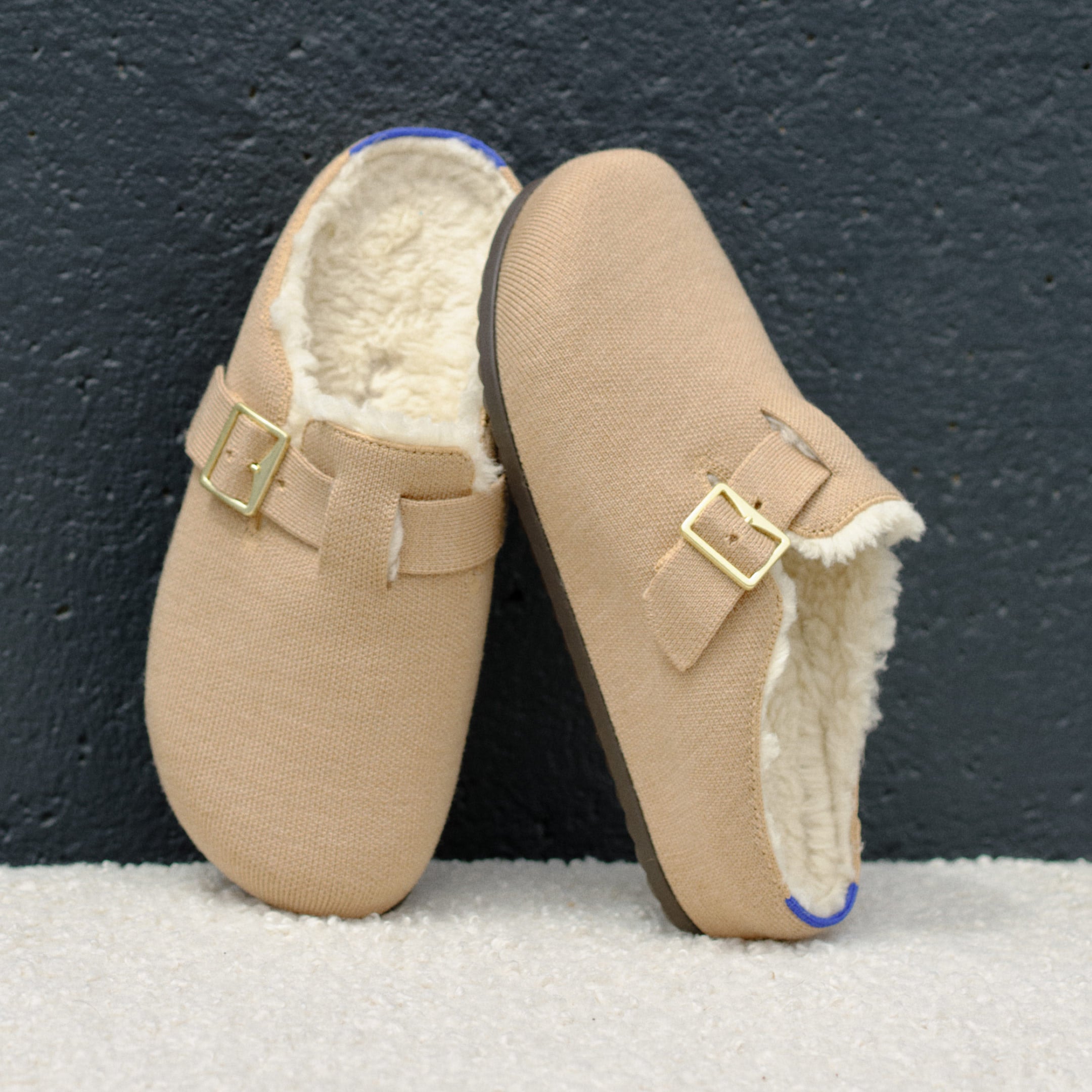 A pair of The Cozy Buckle Clogs against a wall.