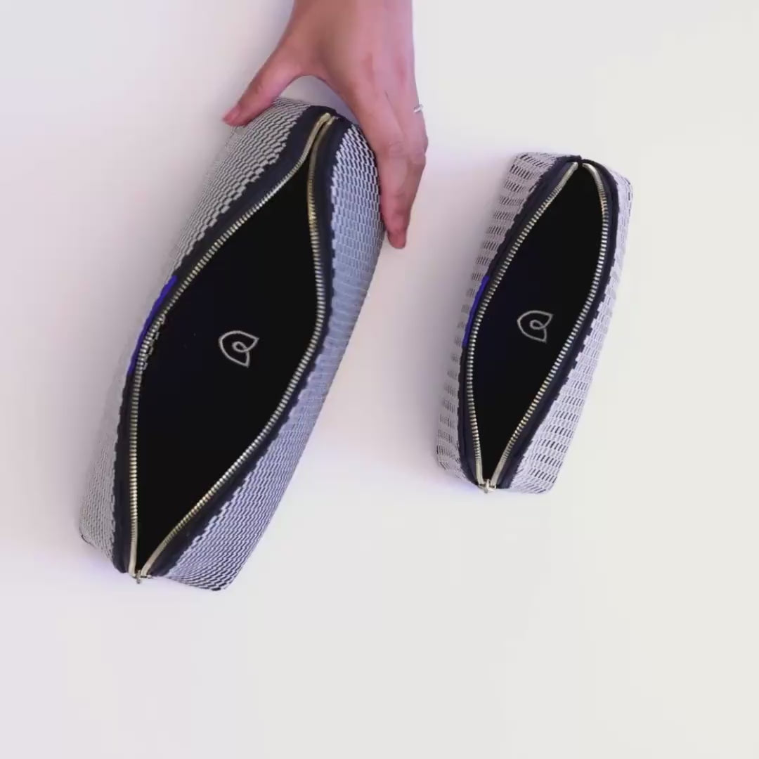 The larger pouch of The Vanity Set in Black and White Micro Check being packed with lotion, sunscreen, a hairbrush, Q-tips, skincare and makeup items, a makeup brush and lipstick. The small pouch is then packed with a hair comb, eye cream, lipstick and some small jewelry items.