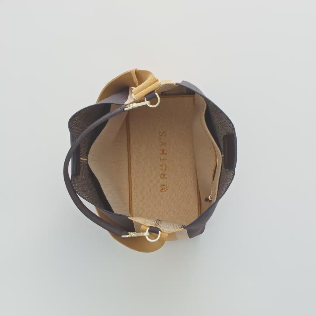 The main compartment of The Bucket Bag in Ink & Ivory being packed with notebooks a 13" laptop, a water bottle, a sweater, an apple and The Vanity Set. The interior zip pocket compartment is packed with a card case, while the other interior slip compartments are packed with sunglasses, keys, a phone, pens and hand sanitizer. The detachable top handle is then removed from the bag.