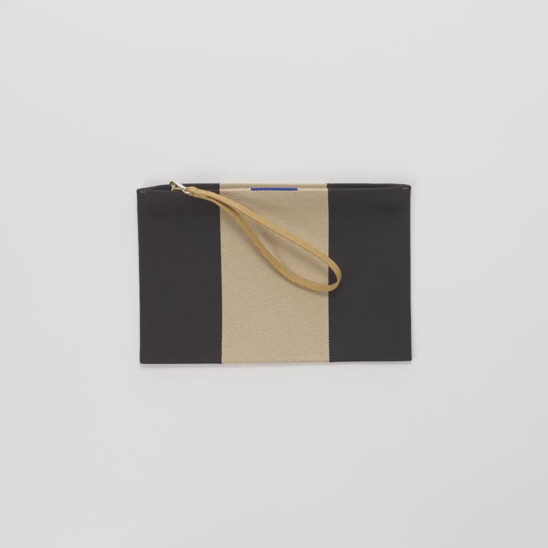 The Wristlet in Ink & Ivory being packed with a passport, card case, phone, pack of gum, AirPods case, lipstick and keys. 