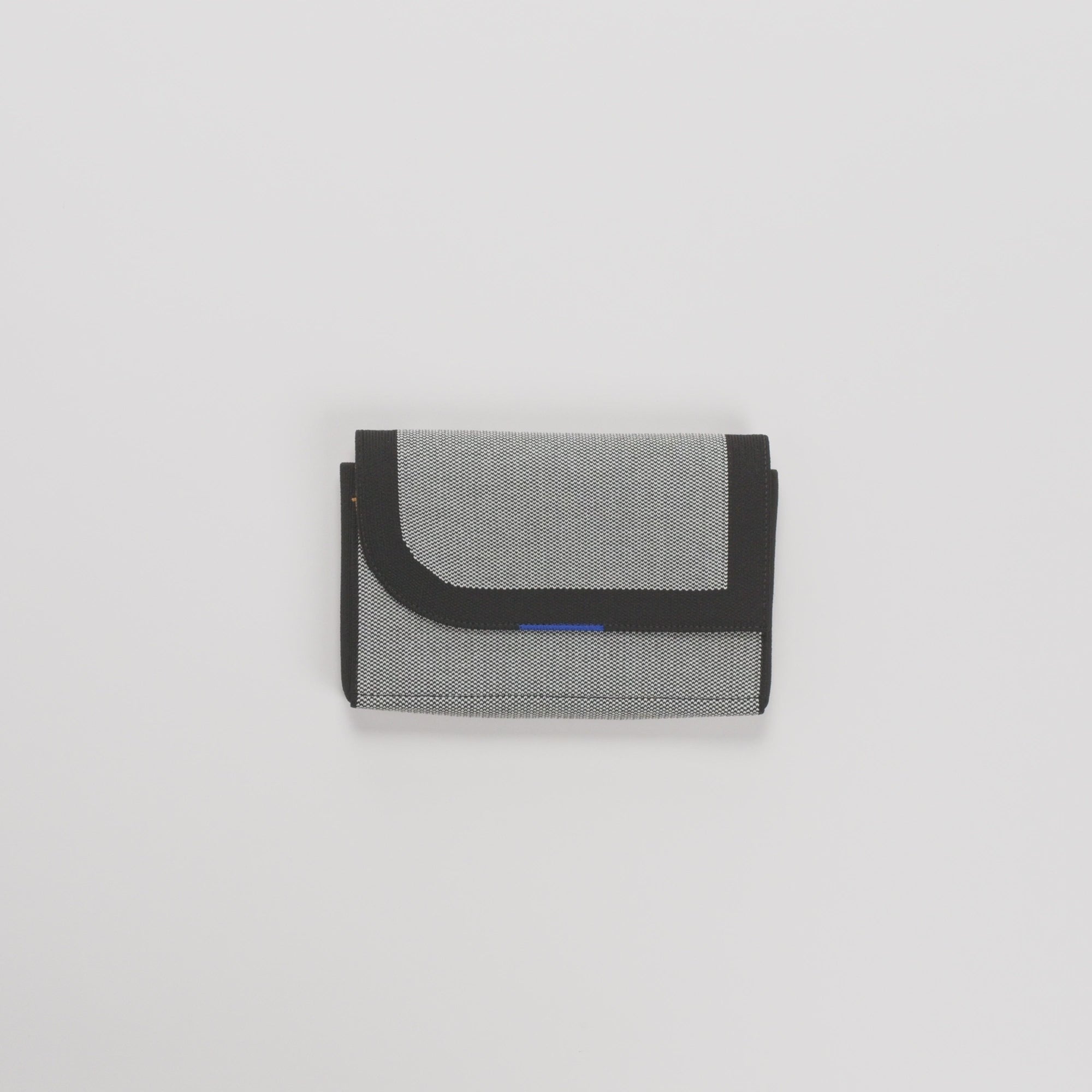 The Belt Bag in Grey Mist being packed, with a card case slotted into the interior slip pocket, and a AirPods case and keys packed into the main compartment. A phone is then slotted into the front slip pocket, and the adjustable, detachable belt is attached to the bag and clipped close.