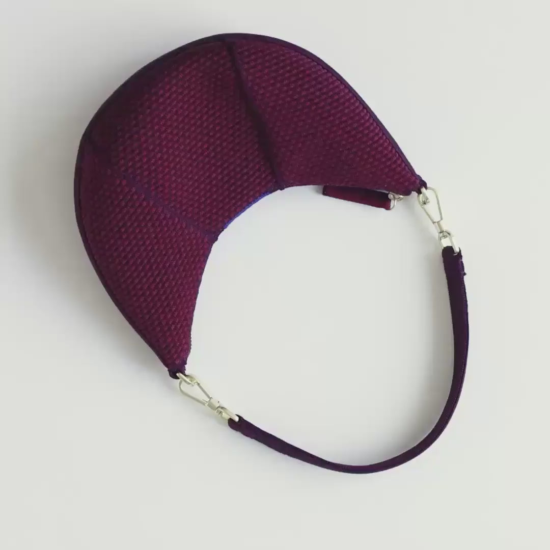 The Mini Crescent Bag in Beet being packed with an iPhone, mints, lipgloss, a bag of snacks and a set of keys. A model zips up The Mini Crescent Bag and carries it out of frame. 