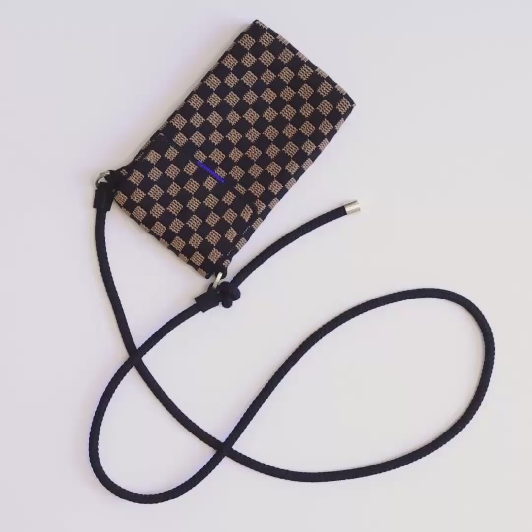 The Phone Crossbody in Midnight Song is opened and packed with cards slipped into the interior pocket, lip balm and an iPhone. The model closes the magnetic flap closure and tightens the cord strap before picking it up and carrying it away. 