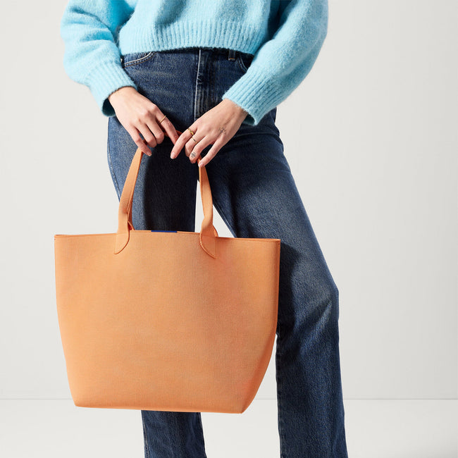 Model holding The Lightweight Tote in Clementine.