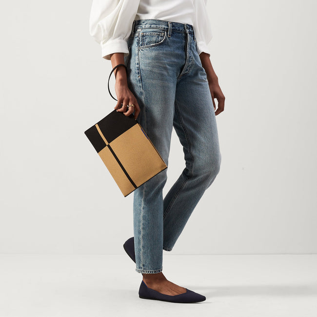 An alternate view of a model holding The Wristlet in Camel and Black. 
