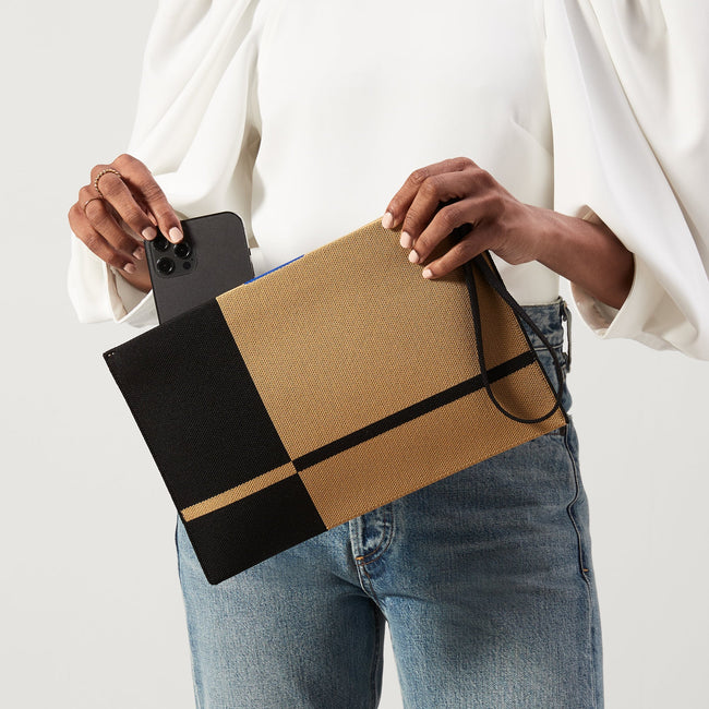 Model holding The Wristlet in Camel and Black. 