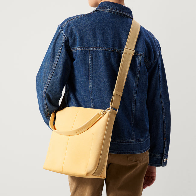 hover | The Mini Zip Bucket in Butter Yellow, carried over the shoulder of a female model, shown from the back.