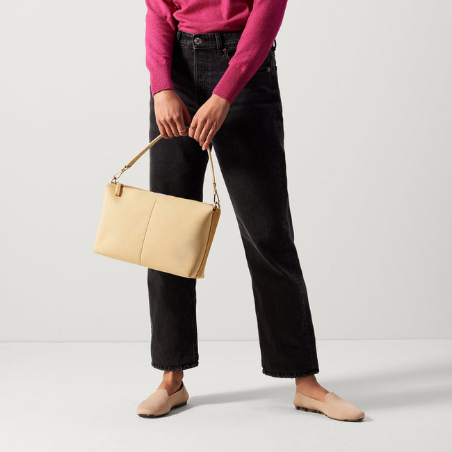 The Daily Crossbody in Golden Wheat, carried by its top handle by a female model.