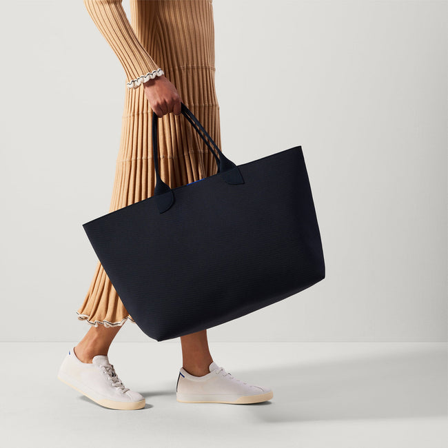 The Lightweight Mega Tote in Navy Twill, carried by its top handles by a model, shown from the front. 