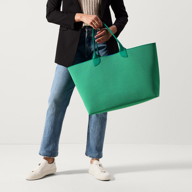 The Lightweight Mega Tote in Sea Green Twill, carried by its top handles by a model, shown from the front.