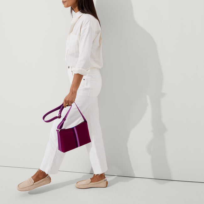 The Casual Crossbody in Plum Stripe, carried by its crossbody strap by a model, shown in motion.